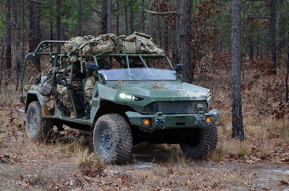 An Infantry Squad Vehicle in a pine forest with soldiers aboard